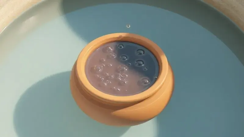 Ilustração de uma panela de barro submersa em água cristalina para o processo de cura natural por hidratação.